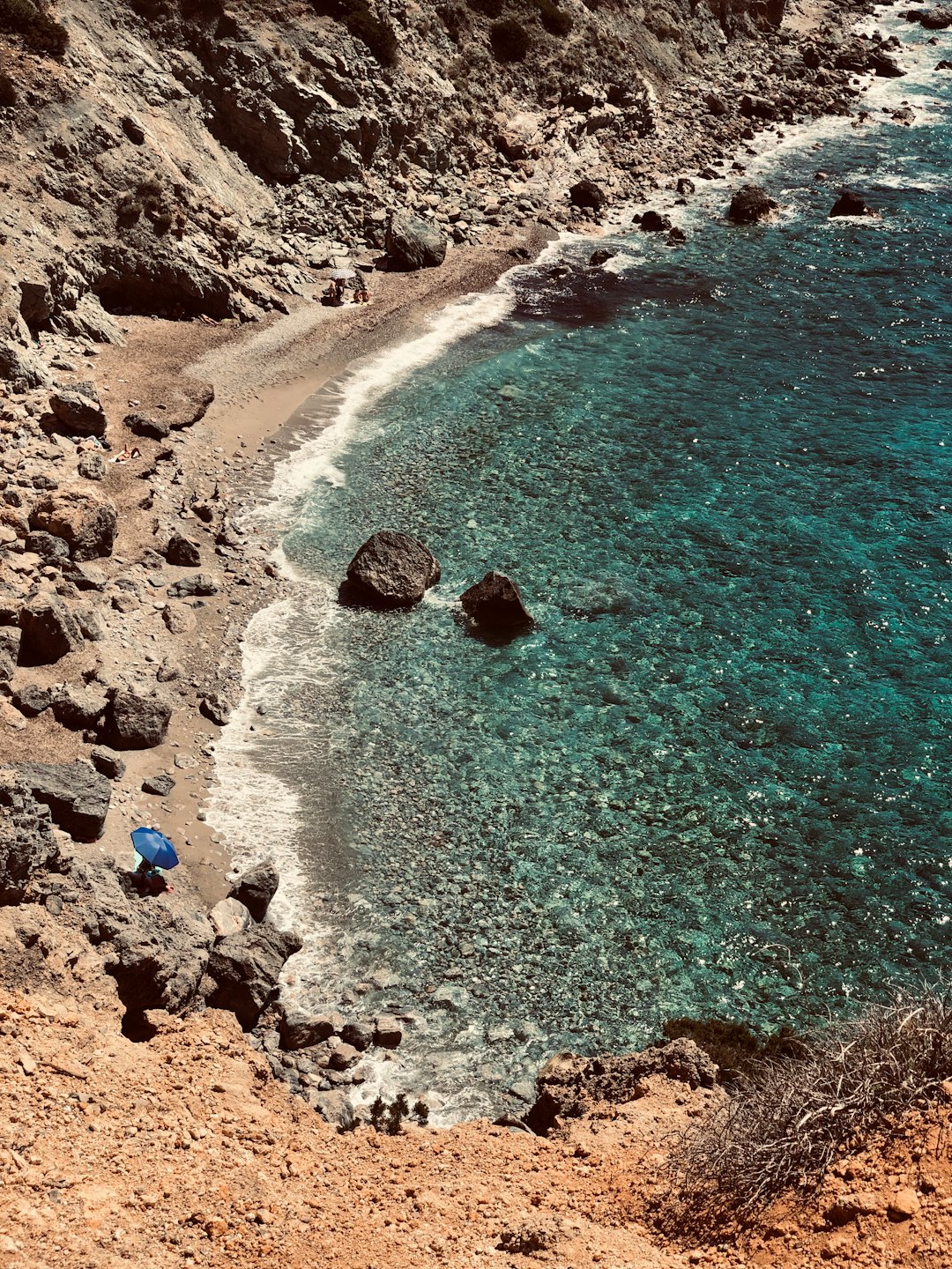 Vista aerea di una caletta rocciosa appartata con acqua turchese e una piccola spiaggia.