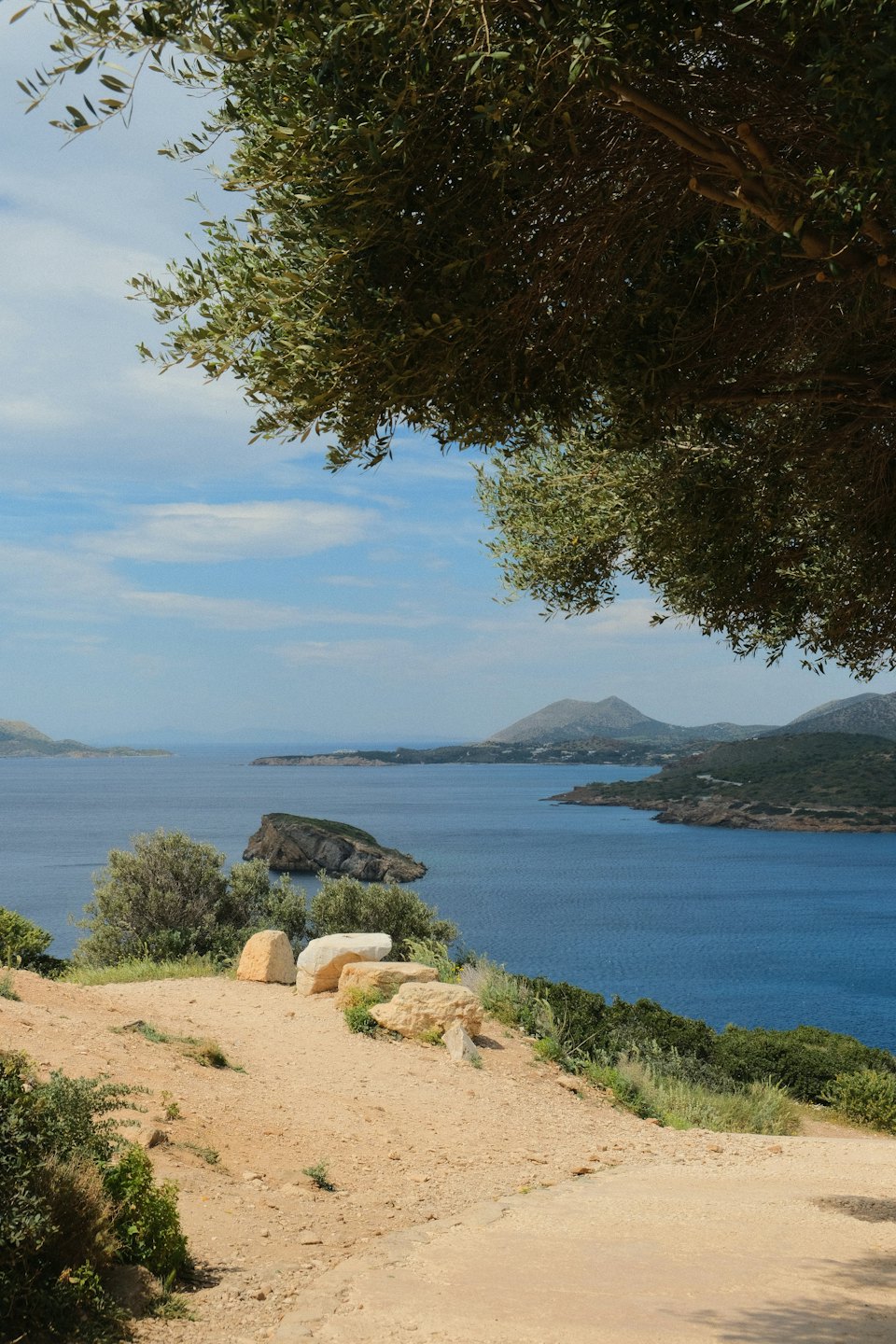 Un sentiero sterrato domina un mare blu con colline verdi.